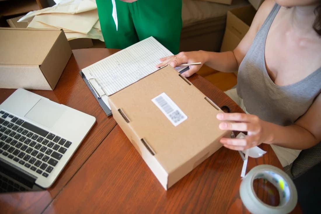 Two people at a small business table packing online orders beside a laptop